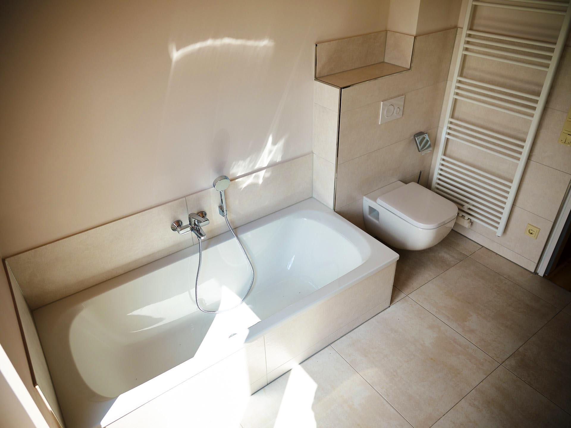 Modernes Badezimmer mit integrierter Badewanne, Wand-WC und Handtuchheizkörper in einer hellen, freundlichen Gestaltung.